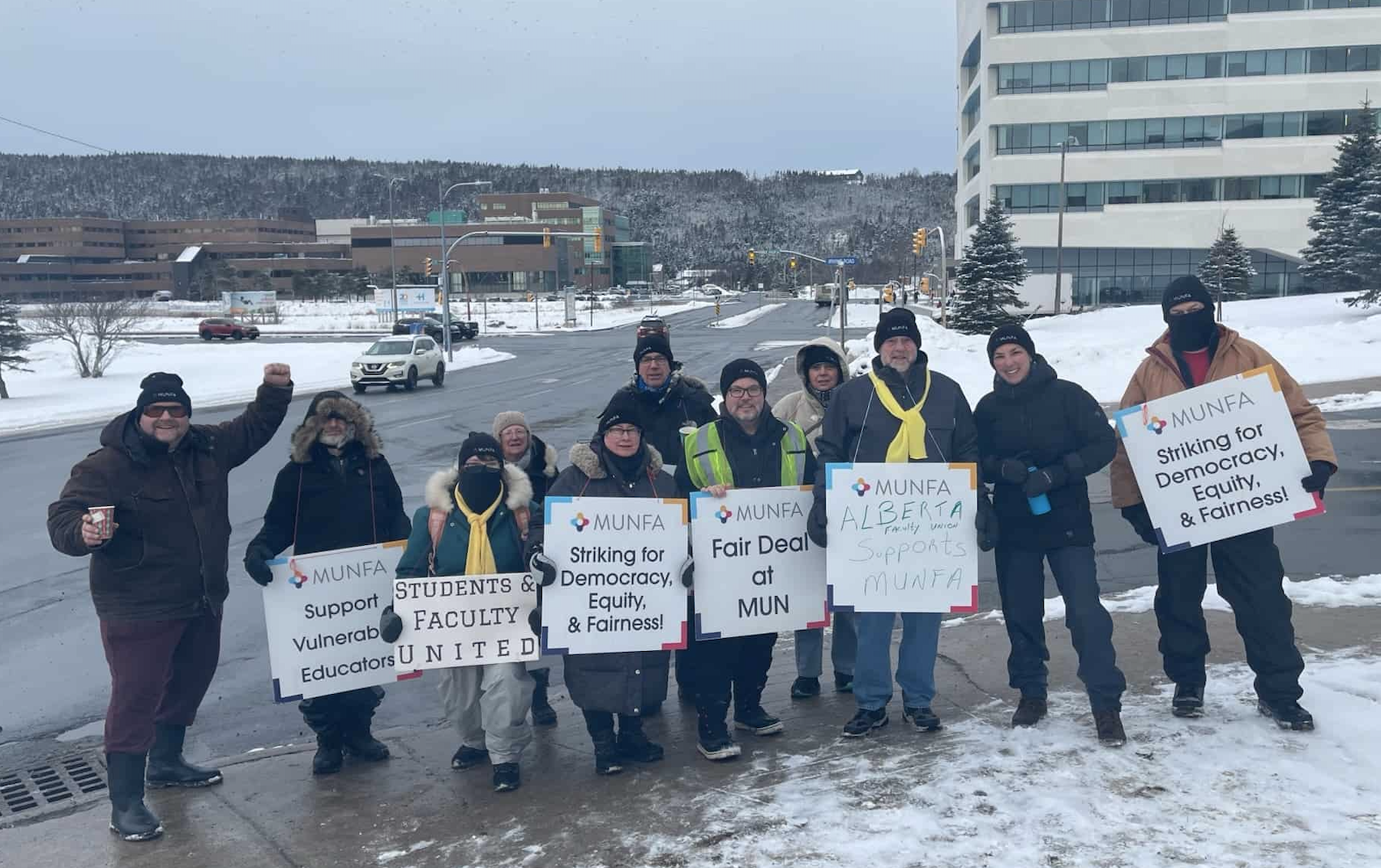 MUNFA picketers stand holding signs on a snowy day in St. John's. The signs advocate for democracy, equity & fairness, supporting vulnerable educators, and a fair deal at MUN